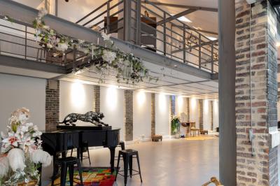 Escalier en bois à côté d'une composition florale blanche, avec un piano et un tapis coloré en arrière-plan.