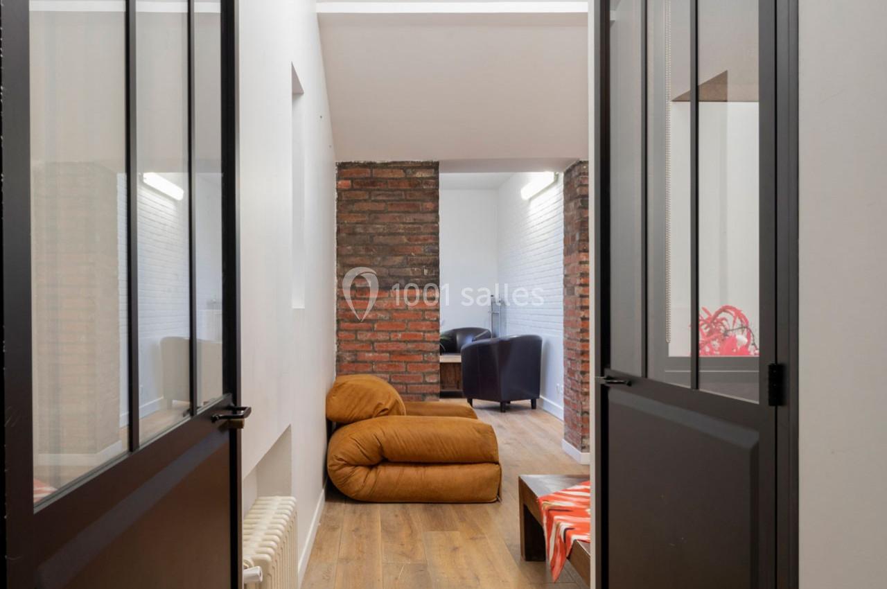 Vue d'un intérieur moderne avec murs en briques, fauteuils, pouf marron et sol en bois clair.