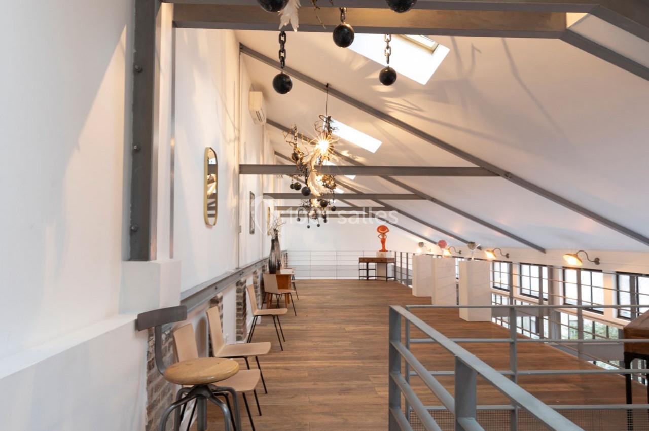 Intérieur d'un espace mansardé lumineux avec parquet, chaises en bois, poutres apparentes et décorations suspendues.