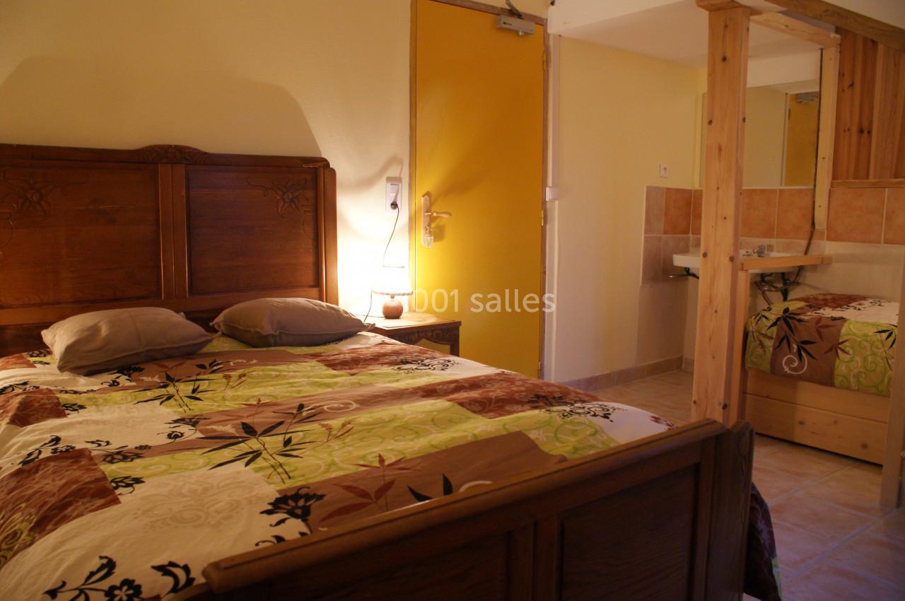 Chambre avec lit double en bois, linge de lit floral, mur jaune, porte fermée et lavabo avec miroir en arrière-plan.