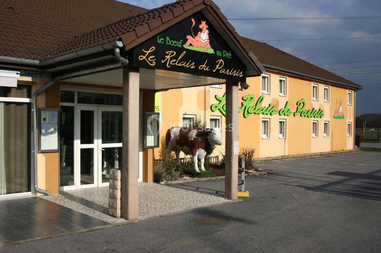 Façade d'un restaurant avec une statue de vache devant l'entrée, bâtiment beige et enseignes visibles.