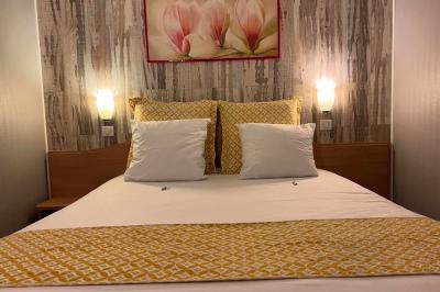 Lit double avec linge de lit jaune et blanc, éclairé par deux appliques murales, devant un tableau de fleurs.