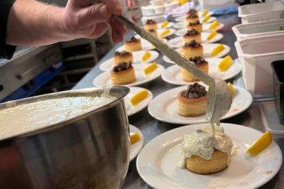 Lit double avec linge de lit jaune et blanc, éclairé par deux appliques murales, devant un tableau de fleurs.