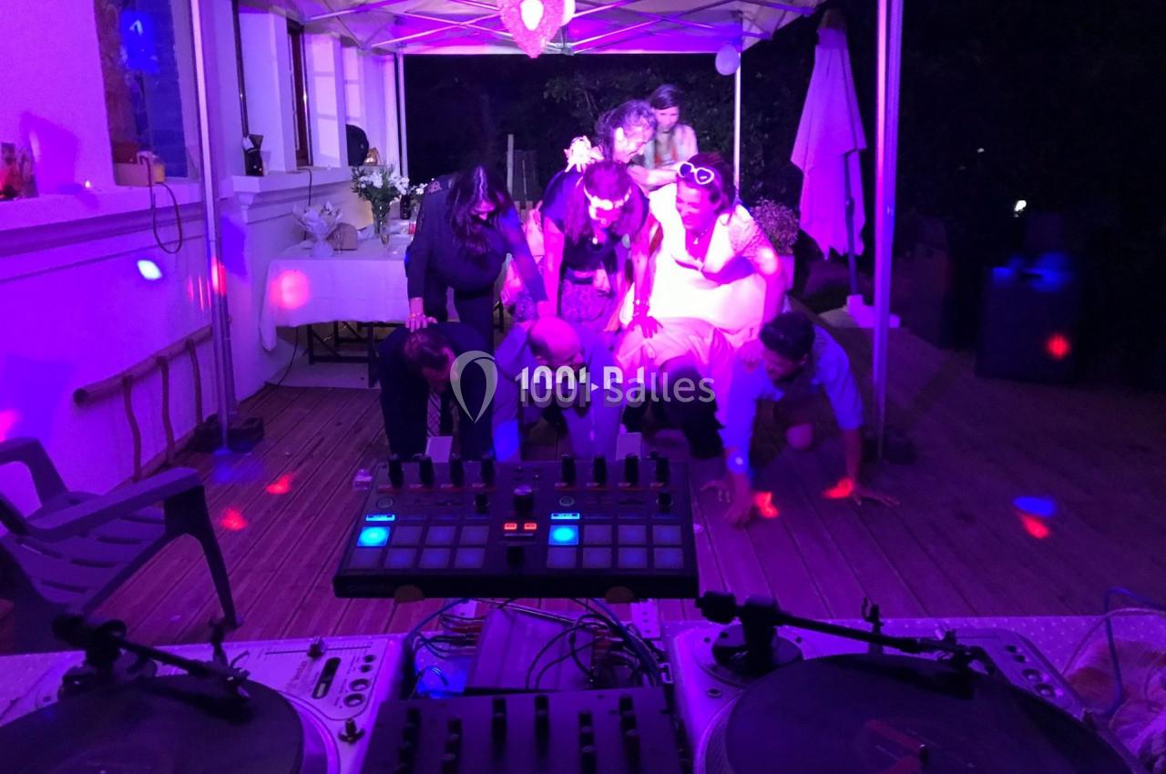 Des personnes dansent sous une tente éclairée par des lumières colorées, avec une table de mixage au premier plan.