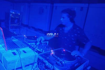 Table de mixage et platines vinyles installées en extérieur, sous des parasols, devant un espace de restauration.