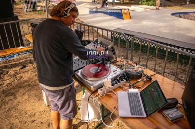 Table de mixage et platines vinyles installées en extérieur, sous des parasols, devant un espace de restauration.