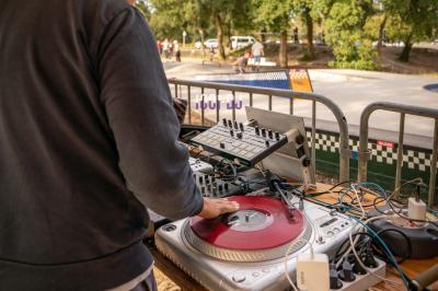 Table de mixage et platines vinyles installées en extérieur, sous des parasols, devant un espace de restauration.