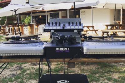 Table de mixage et platines vinyles installées en extérieur, sous des parasols, devant un espace de restauration.