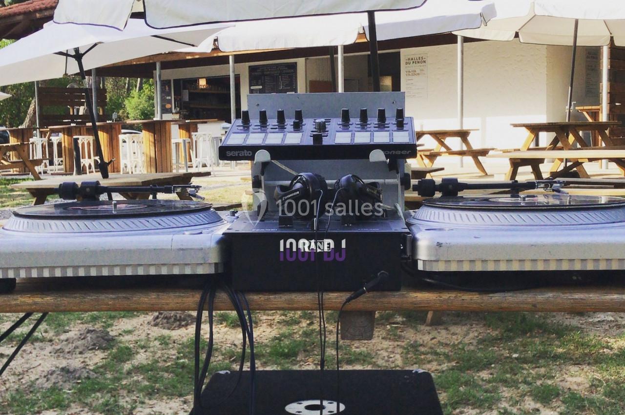 Table de mixage et platines vinyles installées en extérieur, sous des parasols, devant un espace de restauration.