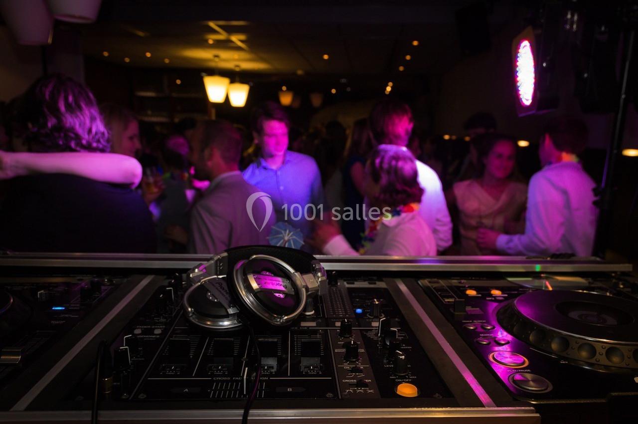 Console de DJ avec casque au premier plan, devant une foule dansante dans une ambiance lumineuse tamisée.