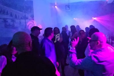 Personnes dansant et discutant dans une salle éclairée par des lumières colorées et une ambiance enfumée.