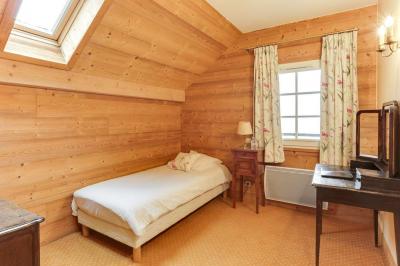 Chambre avec murs en bois, lit simple, bureau, fenêtre avec rideaux fleuris et lumière naturelle.