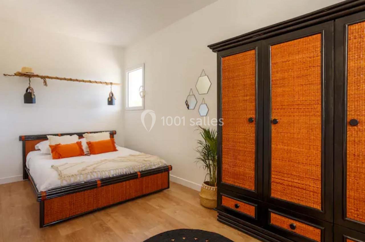 Chambre lumineuse avec lit double, armoire en bois avec panneaux tressés, plantes et miroirs décoratifs au mur.