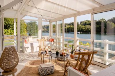 Tables et chaises en bois disposées en extérieur près d'une rivière, avec parasols et végétation en arrière-plan.