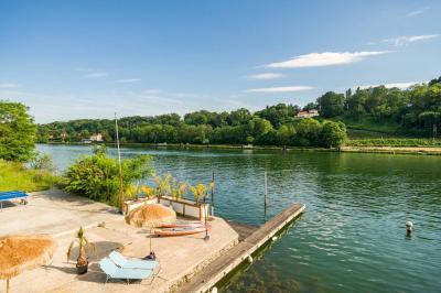 Tables et chaises en bois disposées en extérieur près d'une rivière, avec parasols et végétation en arrière-plan.