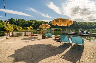 Tables et chaises en bois disposées en extérieur près d'une rivière, avec parasols et végétation en arrière-plan.
