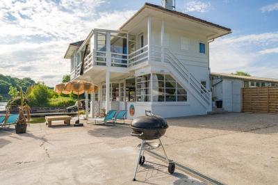 Tables et chaises en bois disposées en extérieur près d'une rivière, avec parasols et végétation en arrière-plan.