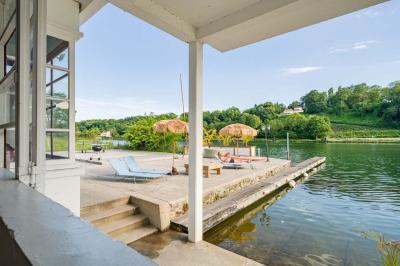 Tables et chaises en bois disposées en extérieur près d'une rivière, avec parasols et végétation en arrière-plan.