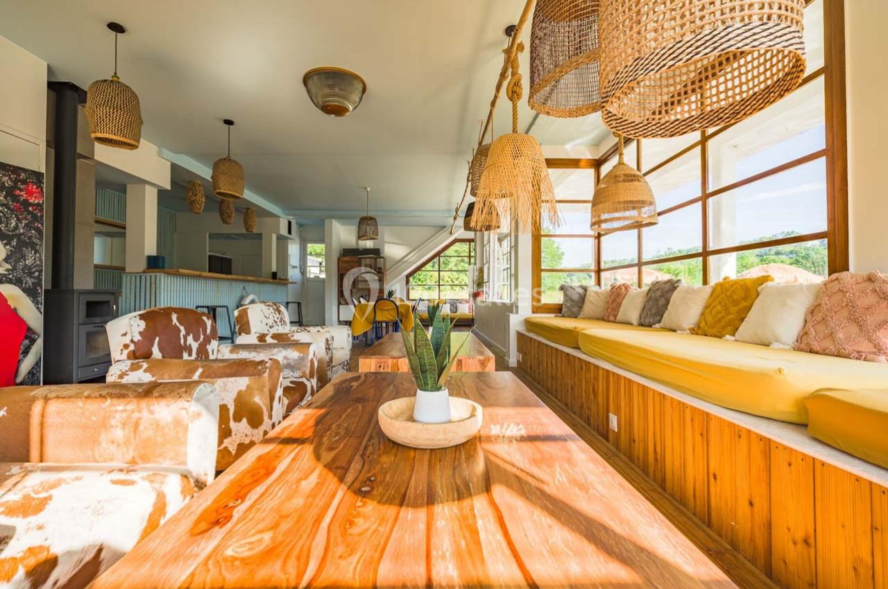 Salle lumineuse avec table en bois, fauteuils à motifs, banquette jaune et suspensions en osier.