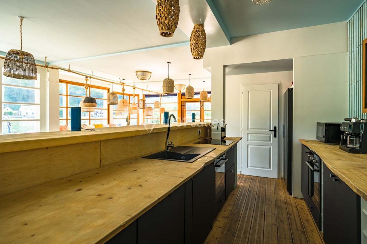 Cuisine moderne avec plan de travail en bois, évier noir, électroménagers intégrés et luminaires suspendus en osier.