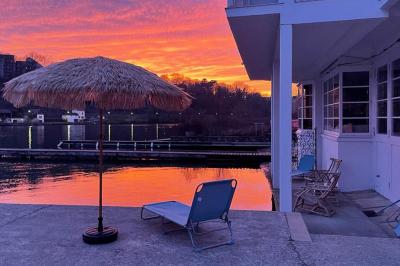 Tables et chaises en bois disposées en extérieur près d'une rivière, avec parasols et végétation en arrière-plan.