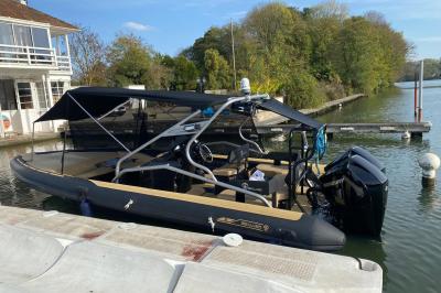 Tables et chaises en bois disposées en extérieur près d'une rivière, avec parasols et végétation en arrière-plan.