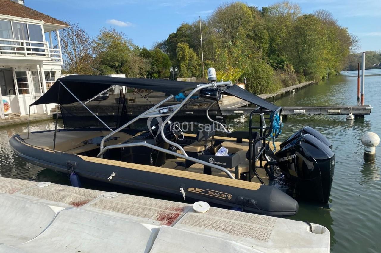 Bateau semi-rigide noir amarré à un quai, équipé d'un moteur hors-bord et d'un toit d'ombrage.