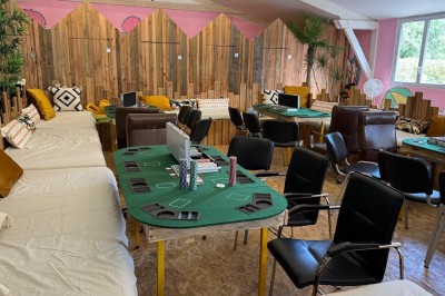 Tables et chaises en bois disposées en extérieur près d'une rivière, avec parasols et végétation en arrière-plan.