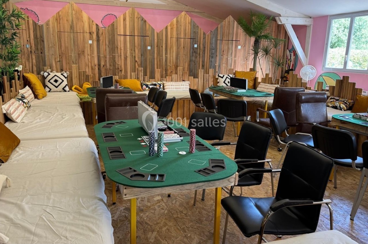 Salle aménagée avec des tables de jeu de cartes, des chaises, des canapés et une décoration chaleureuse en bois et plantes.