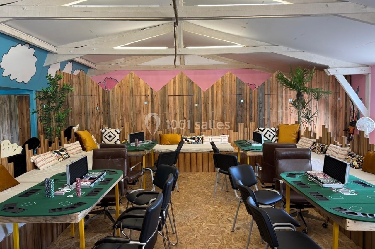 Salle aménagée avec des tables de jeu vertes, des chaises noires et des décorations murales colorées en bois et peinture.