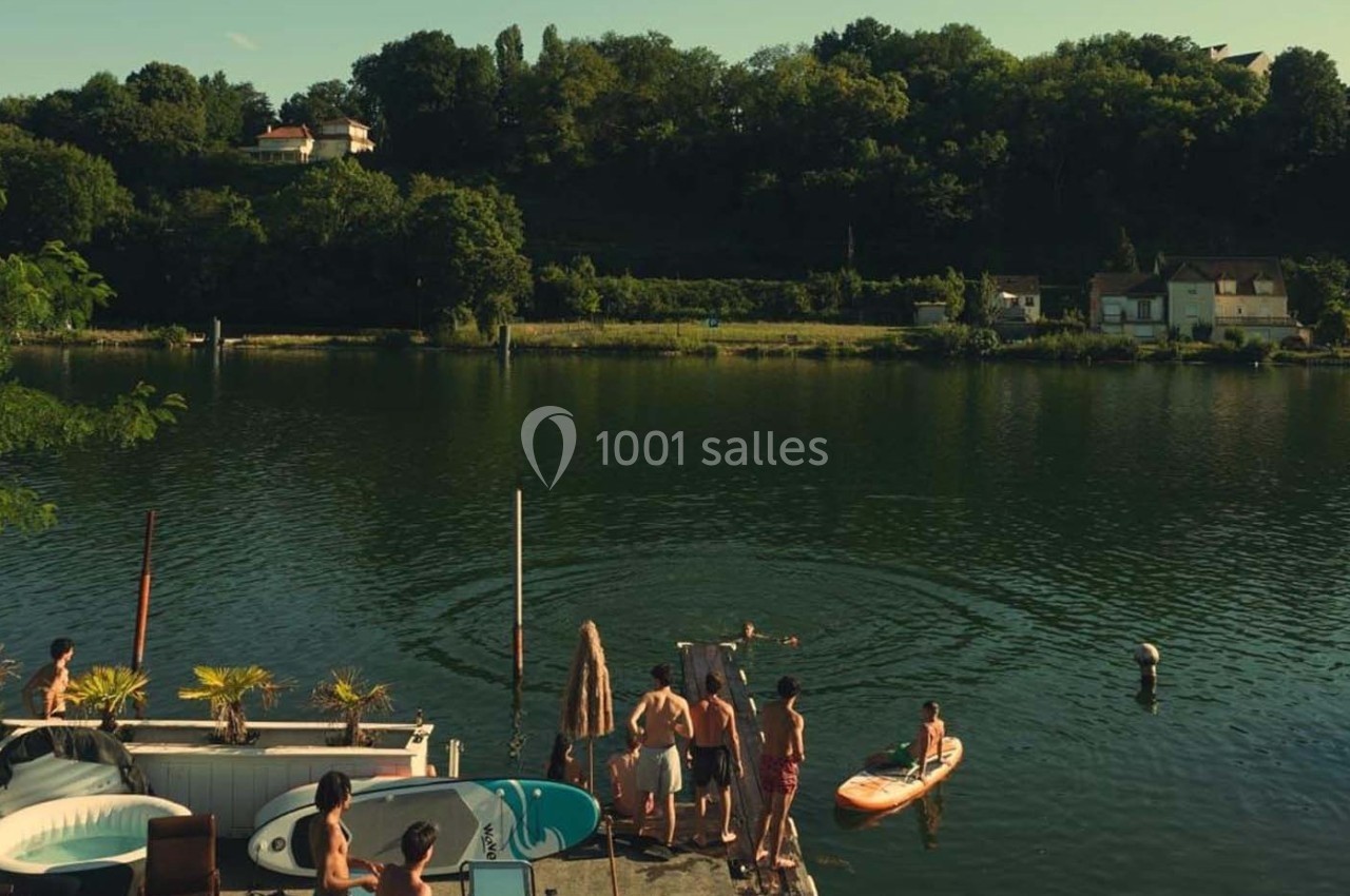 Des personnes profitent d'une journée ensoleillée près d'un ponton au bord d'une rivière, entourée de verdure.