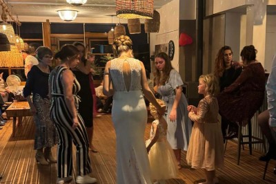 Tables et chaises en bois disposées en extérieur près d'une rivière, avec parasols et végétation en arrière-plan.