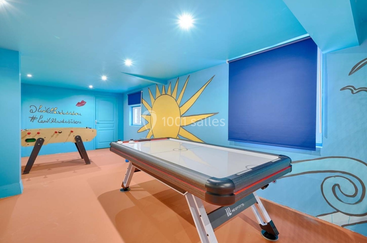 Salle de jeux colorée avec une table d'air hockey, un baby-foot et des murs décorés de motifs ensoleillés.