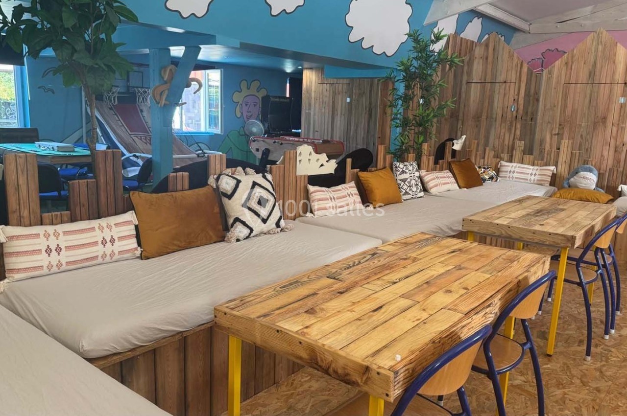 Banquettes avec coussins colorés et tables en bois dans un espace intérieur décoré de fresques et de plantes.