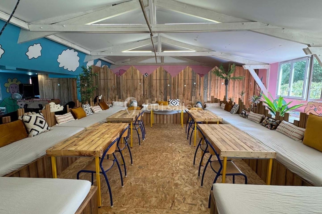 Salle lumineuse avec tables en bois, bancs garnis de coussins et décorations murales colorées.
