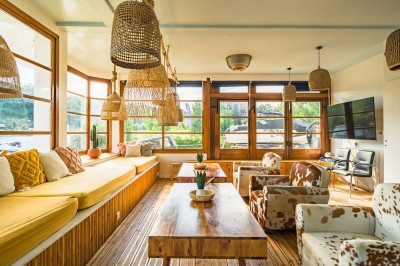 Tables et chaises en bois disposées en extérieur près d'une rivière, avec parasols et végétation en arrière-plan.