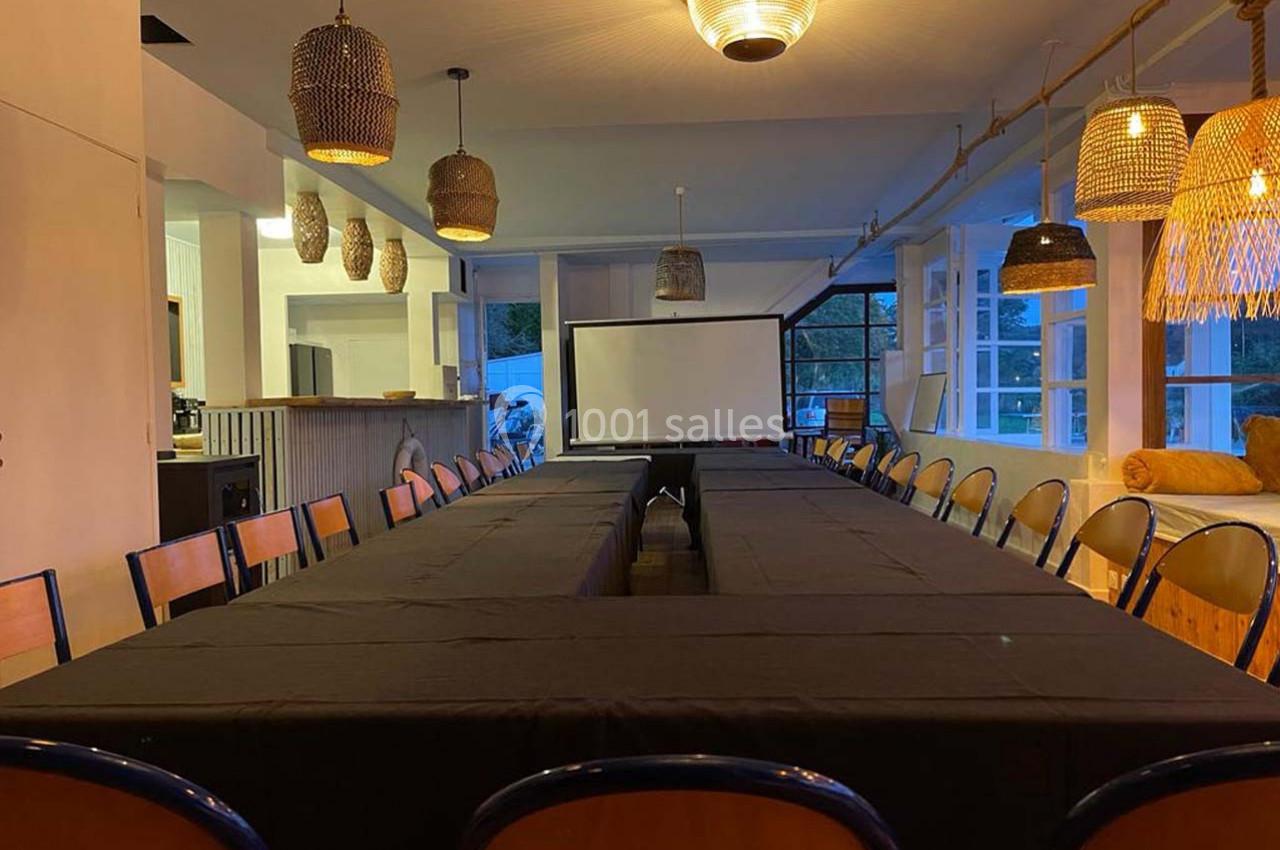 Salle de réunion avec une grande table en U, chaises alignées, éclairage chaleureux et écran de projection au centre.