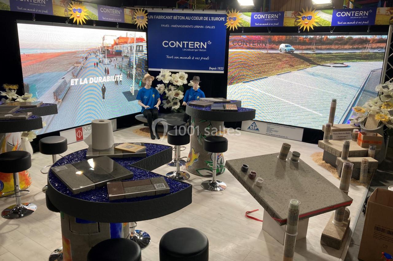 Stand d'exposition présentant des produits en béton, avec écrans, échantillons et décorations sur des tables.