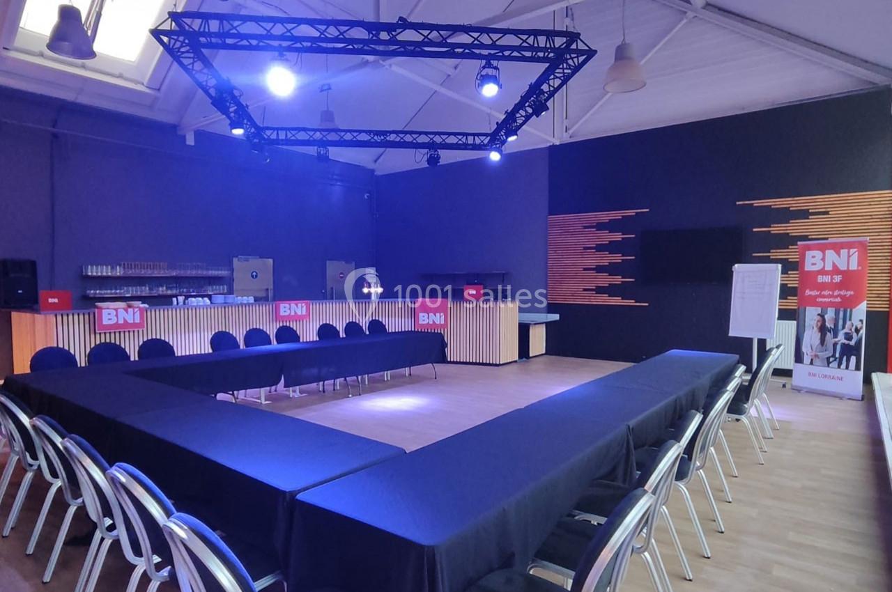 Salle de réunion avec tables disposées en U, chaises alignées, éclairage bleu et panneaux ’BNI’ en arrière-plan.