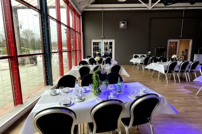 Salle de réception décorée avec des guirlandes lumineuses, tables dressées et éclairage tamisé bleu et rose.