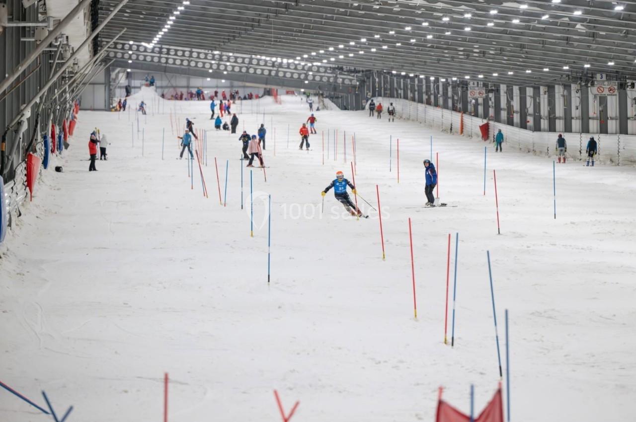 Des skieurs s'entraînent sur une piste intérieure balisée de piquets colorés sous un éclairage artificiel.