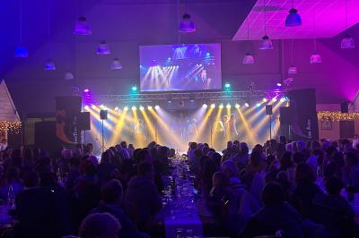 Salle de réception décorée avec des guirlandes lumineuses, tables dressées et éclairage tamisé bleu et rose.