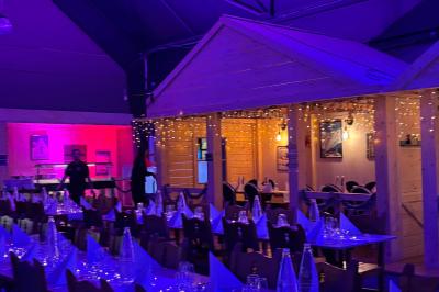 Salle de réception décorée avec des guirlandes lumineuses, tables dressées et éclairage tamisé bleu et rose.