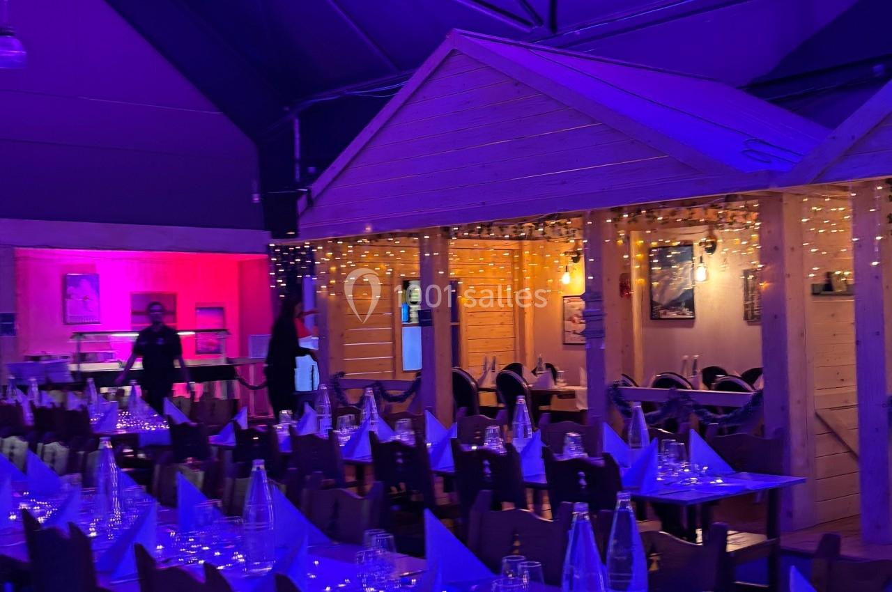 Salle de réception décorée avec des guirlandes lumineuses, tables dressées et éclairage tamisé bleu et rose.