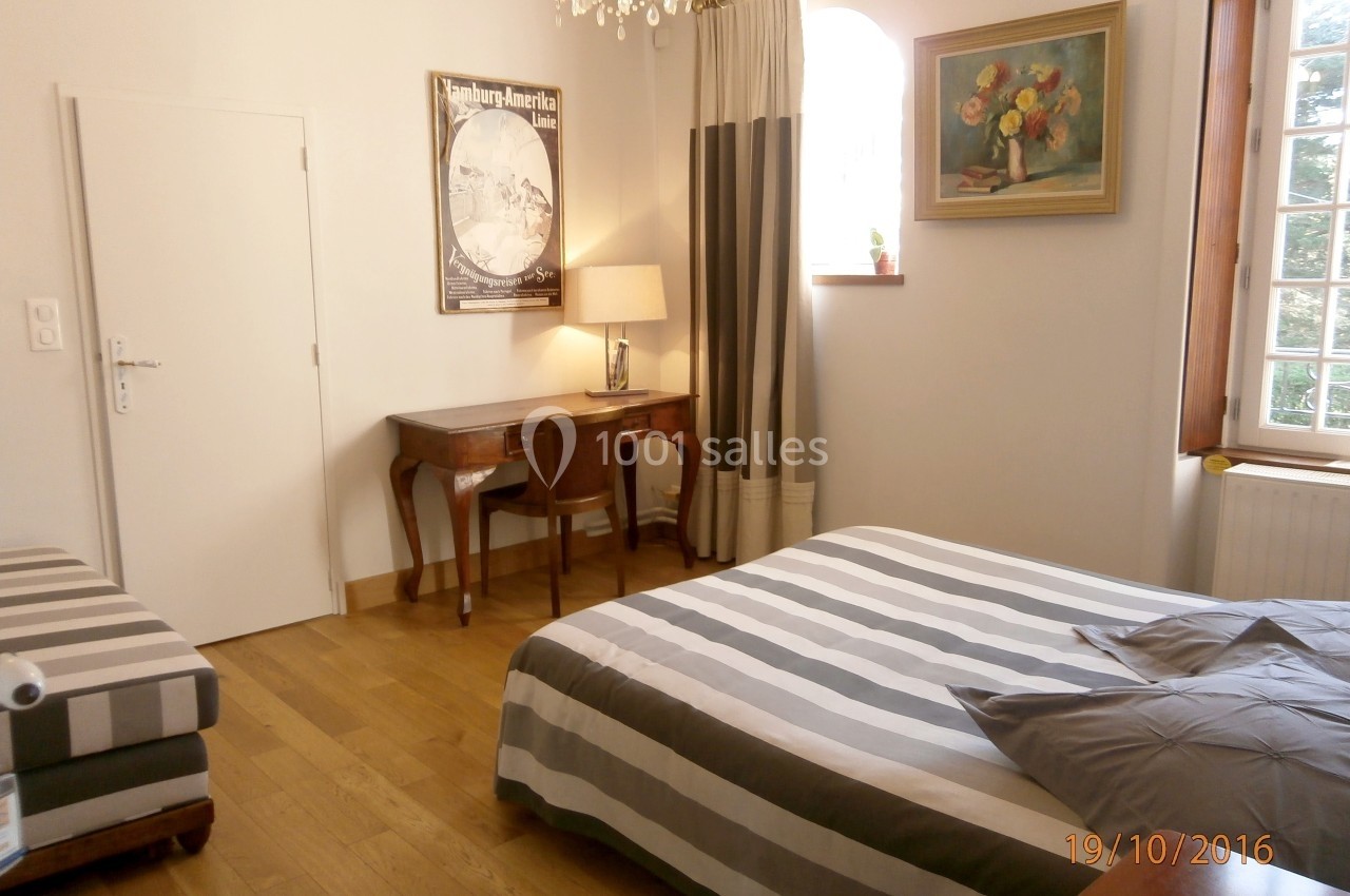 Chambre lumineuse avec lit à rayures, bureau en bois, lampe, tableau floral et fenêtre à rideaux.