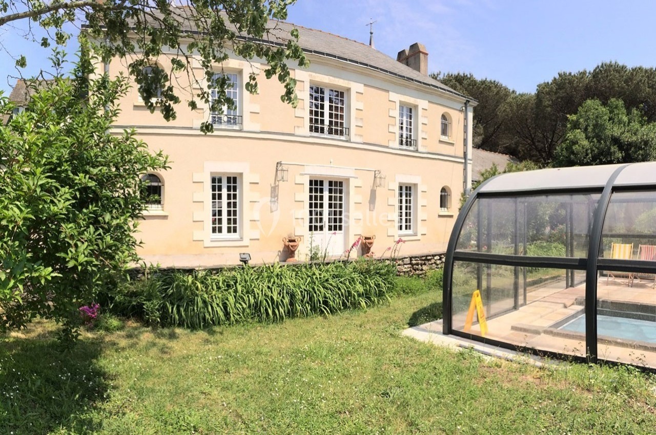 Maison en pierre avec jardin verdoyant et piscine couverte sous un ciel dégagé.
