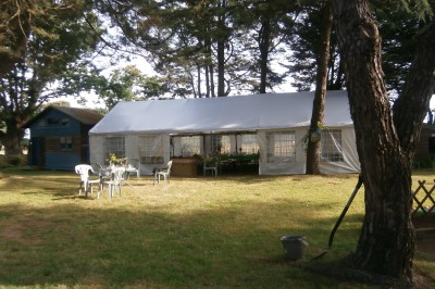 Personnes rassemblées sous une tente blanche lors d'un événement en extérieur, discutant et se servant des boissons.