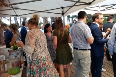 Personnes rassemblées sous une tente blanche lors d'un événement en extérieur, discutant et se servant des boissons.