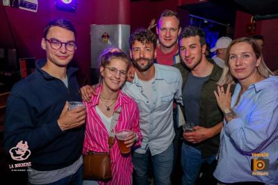 Un homme souriant avec des lunettes de soleil pose avec une femme dans un environnement festif et animé.