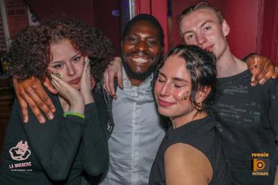 Un homme souriant avec des lunettes de soleil pose avec une femme dans un environnement festif et animé.